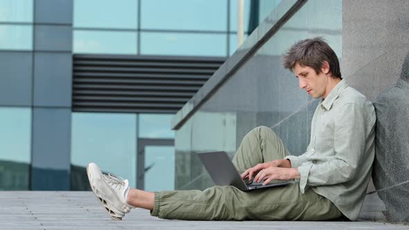 Focused Young Man Wearing Casual Clothes and Sneakers Using Laptop Typing on Keyboard Writing Email