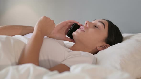 Latin Woman Talking on Smartphone Laying in Bed 