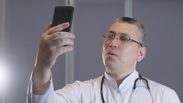 male doctor smiles and grimaces while taking a selfie on his phone