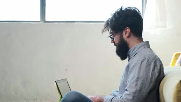 Man Working at the Computer with a Lot of Reminder Notes Sitting Near Sofa