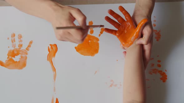 Mom Paints Children's Hands with Paints and the Child Puts a Handprint on the Paper