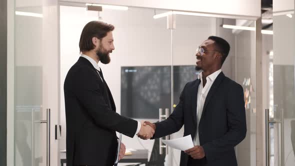 Two Smiling Businessmen Shaking Hands Together While Standing in an Office