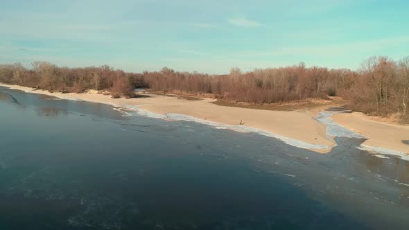 Aerial Drone Footage of Flight Over a Sandy Shore with a Small River in Winter