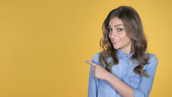 Young Girl Pointing with Finger on Side Yellow Background