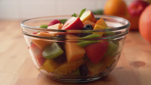 Camera follows putting fresh mint over fruit salad. Slow Motion.