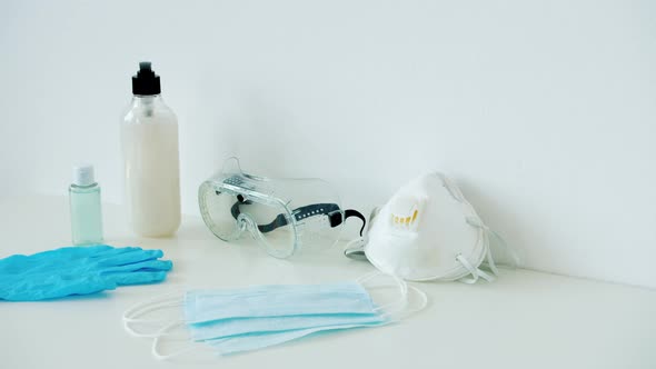 Sanitizer, Face Mask, Respirator, Rubber Gloves and Goggles on White Table Indoors