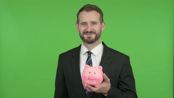 Cheerful Businessman Putting Money in Piggy Bank Against Chroma Key