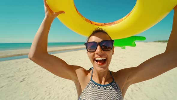 Smiling Girl on Sunny Ocean Beach Looking at Camera Through Yellow Inflattable Ring with Funny Face