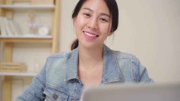 Asia woman feeling happy smiling and looking to camera using laptop on desk in living room at home.