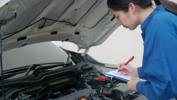 Asian female mechanic examining car