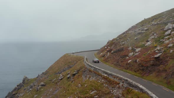 Forwards Tracking of Black Car Driving on Narrow Exposed Coastal Road High on Cliff