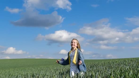 Cute and Happy Girl Joyfully Runs in a Wheat Field with a Bouquet of Flowers