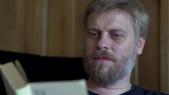 Adult Handsome Man with Beard Is Reading Book, Closeup Portrait