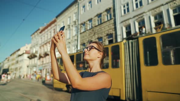 Woman Stands on an Old Street and Takes a Photo or Video on a Smartphone at Sunset