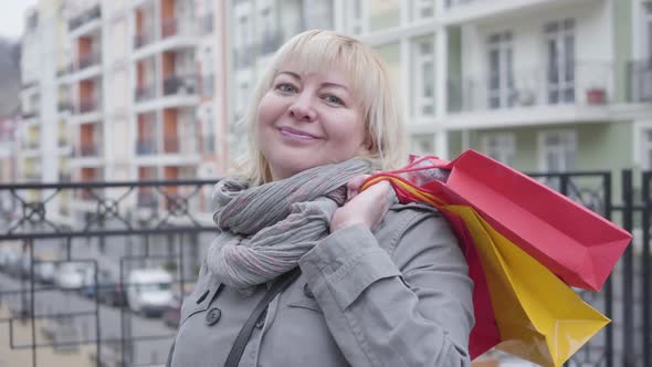 Close-up Portrait of Happy Senior Caucasian Woman Standing with Shopping Bags Outdoors. Nice