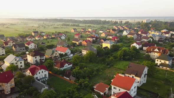 Aerial view of rural residential area with private homes between green fields at sunrise.