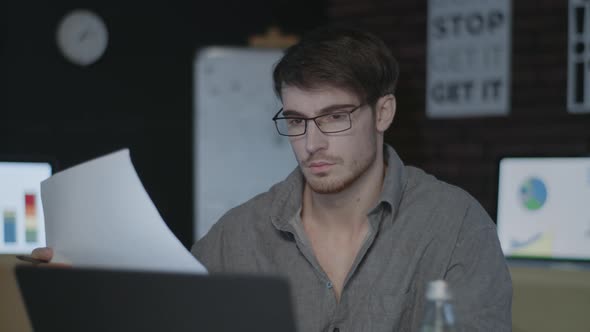 Thoughtful Business Man Working with Document Near Computer in Dark Office