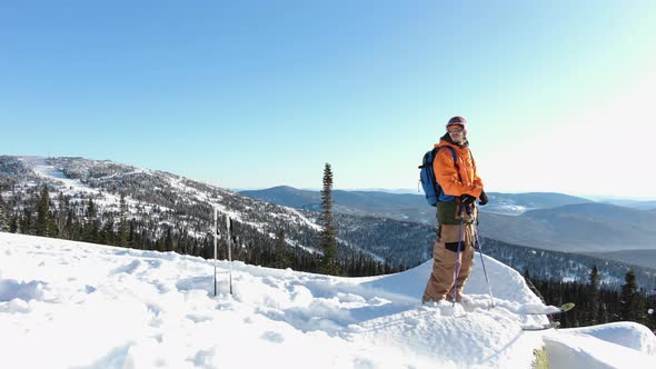 Guy with Ski Equipment Stands on Snowy Hill Edge Upper