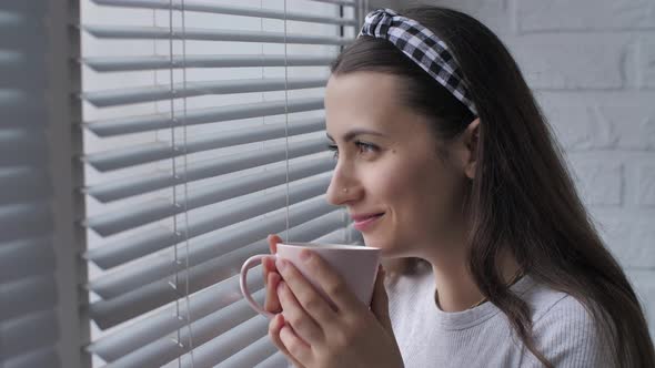 Woman with Cup Looks Outside the Window