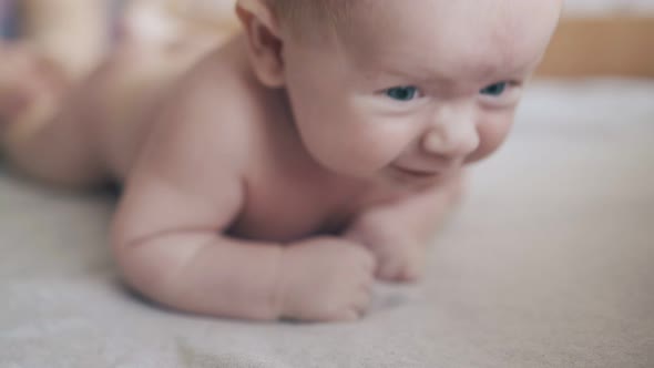 Newborn Boy with Blue Eyes and Plump Cheeks Lies on Stomach