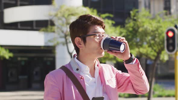 Asian man drinking coffee and using smartphone while crossing the street