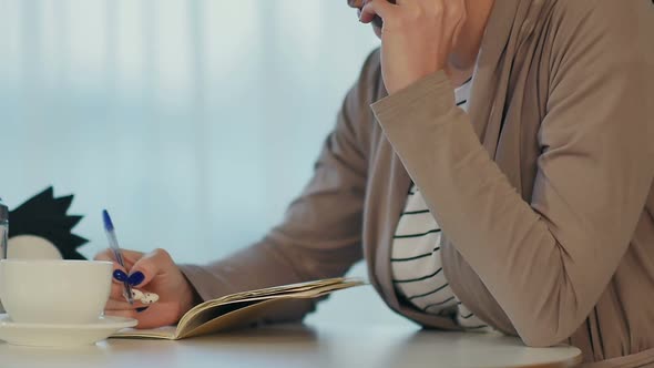 Business Woman Talking on the Phone and Making Notes in a Cafe During Coffee Break