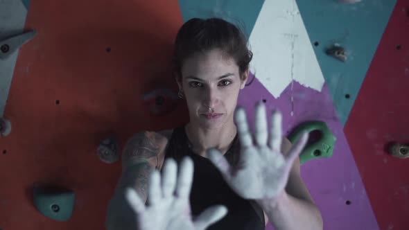 Strong Woman Shows Hands Covered with Magnesium Powder for Climbing in Front of Artificial Rock Wall