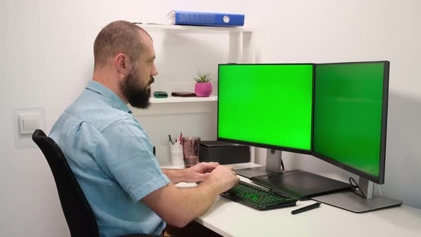 Bearded man drinking water from a glass sitting at a table in front of two green chroma key screens