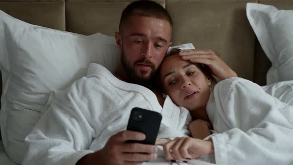 Married Couple is Lying in Bed and Watching Pictures in Smartphone Man and Woman in Hotel