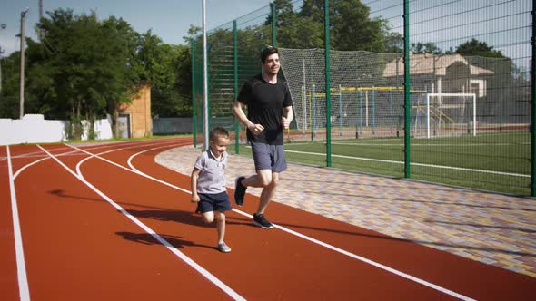 Father and His Kid Boy in Sportswear are Smiling and Running By the Track