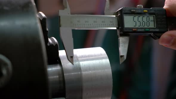 Worker measuring an aluminum metal piece on lathe with calliper