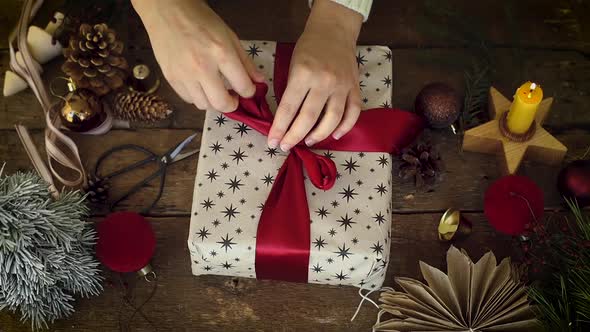 Hands wrapping stylish Christmas gift with red ribbon on rustic wooden table