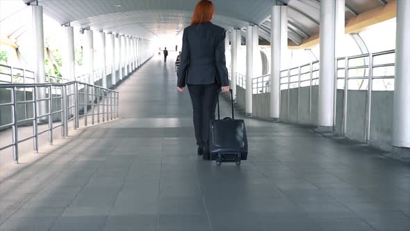 Young Attractive Business Woman Dragging a Wheeled Suitcase at the Airport for Business Trip