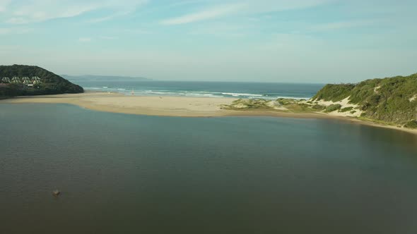 Aerial of river mouth streaming towards ocean waves on sandy beach