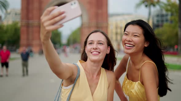 Two Happy Mixedrace Women Friends Making Selfie Outdoors and Choosing Best Photo on Mobile Phone