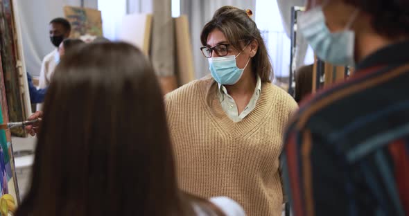 Mature teacher working with students while wearing safety masks during painting class at school