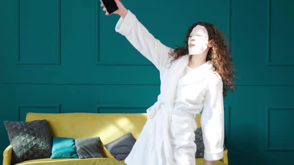 Happy Woman in Bathrobe and with Mask on Face is Dancing Alone Listening Music