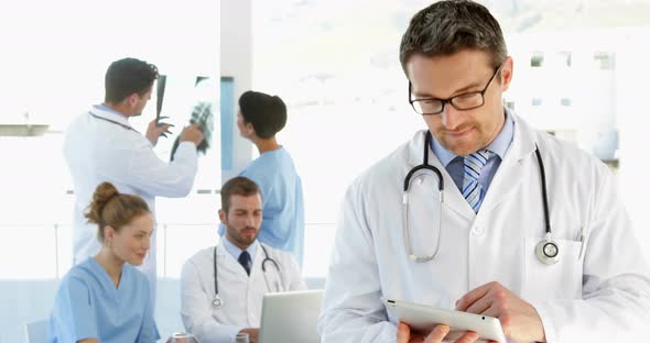 Doctor Using Tablet While Staff are Working Behind Him