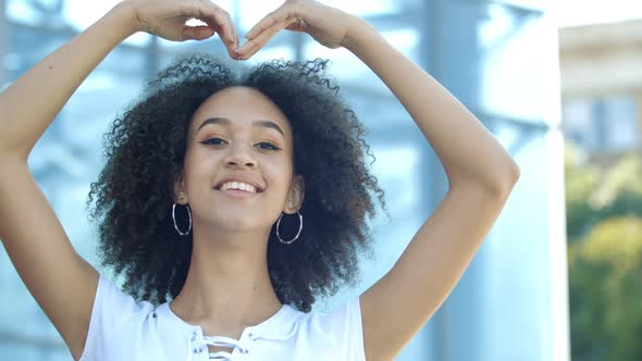 Smiling Young Woman Shows Sign in Shape of Large Heart Her Hands. Concept of Charity, Help, Love