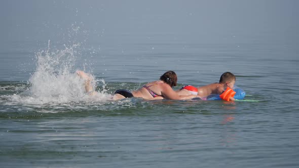 Family Vacation at the Sea. Boys on an Air Mattress, in Flippers Dressed on Their Hands, Surf the