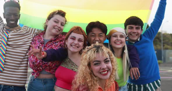 Young diverse people having fun holding LGBT rainbow flag outdoor