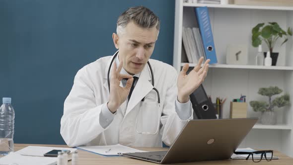 Caucasian male doctor using laptop for online meeting with patient, listens to complaints