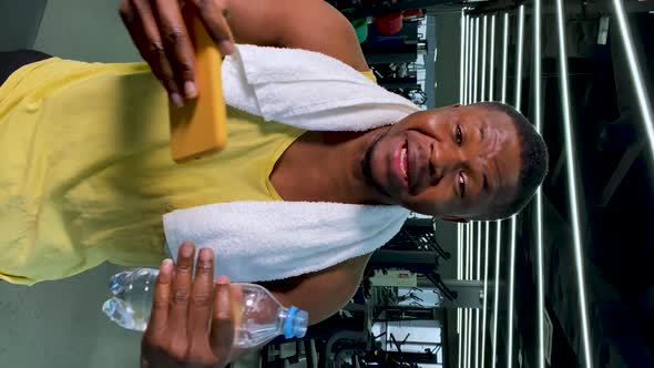 A Strong Black Athlete in the Gym Holds the Phone and with Enthusiasm Tells Something Pointing to
