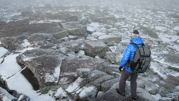 Unidentified Tourist with Backpack Going Down the Mountain on Frozen Stones