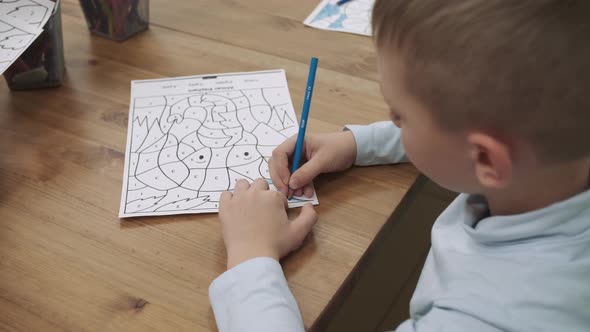 A Student Boy Paints a Drawing with a Colored Pencil While Sitting at the Table