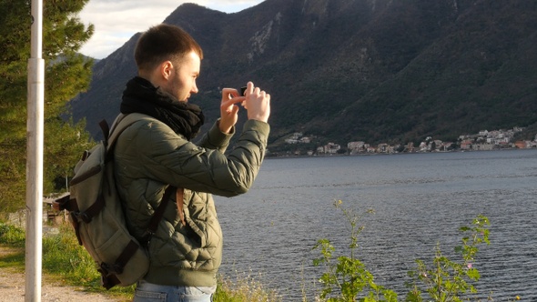 Male tourist is watching seascape and taking pictures using