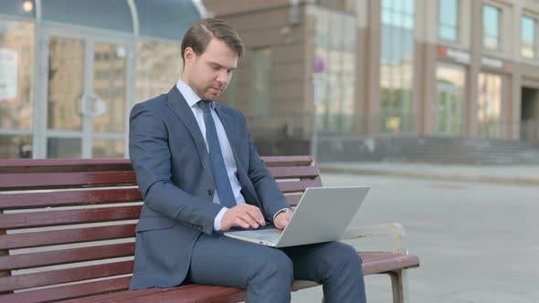 Businessman Celebrating Success on Laptop while Sitting Outdoor on Bench