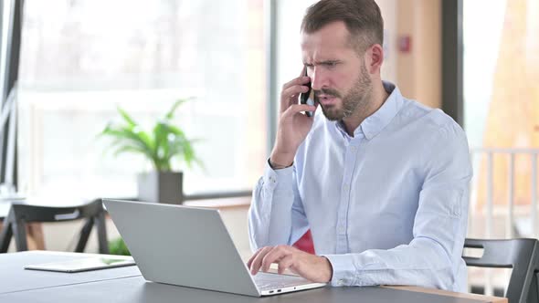 Furious Young Man Talking on Smartphone in Office 