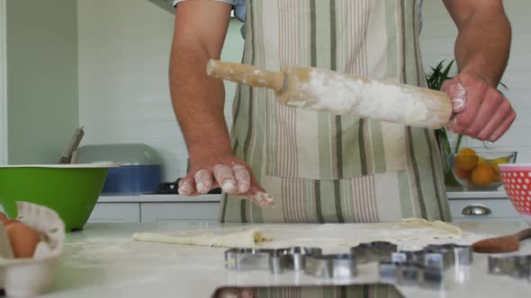 Midsection of caucasian man rolling dough for baking in kitchen