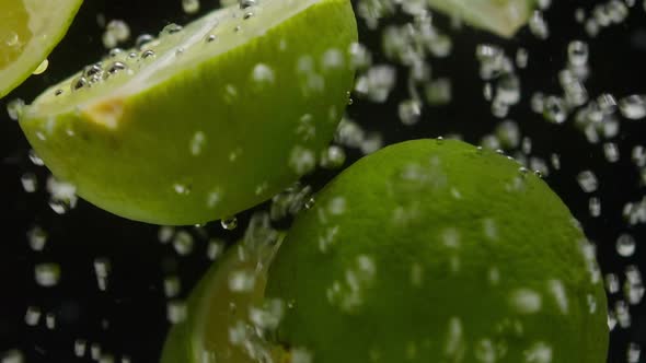 Closeup of Falling Ripe Limes Into the Sparkling Water on Black Background Making a Cocktail of